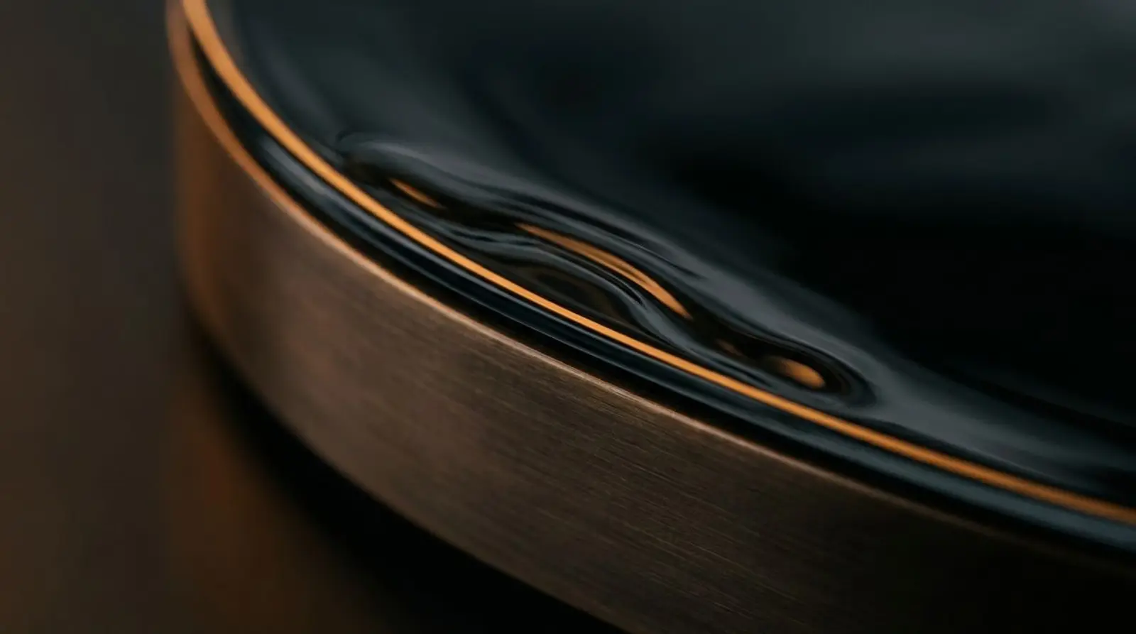 Abstract macro of dark glass over brushed bronze with a line of warm light.